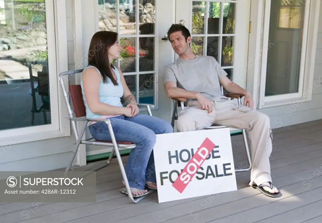Couple Sitting With a House For Sale Sold Sign
