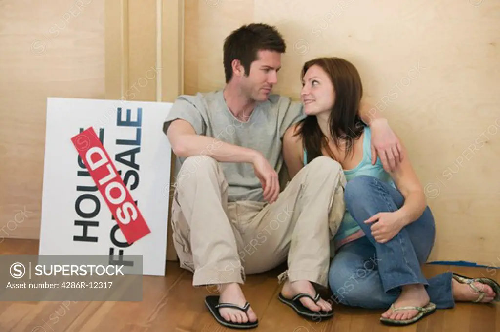 Couple Sitting With a House For Sale Sold Sign