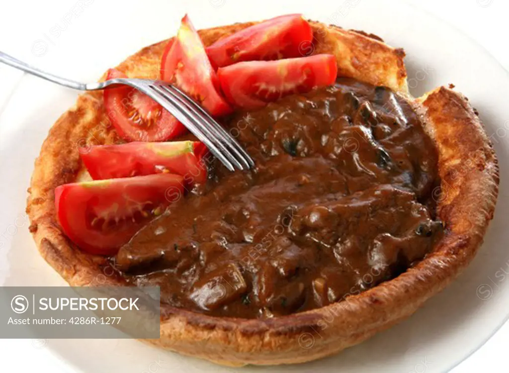 A big yorkshire pudding filled with stewed beef and mushrooms in gravy, topped off with wedges of tomato.