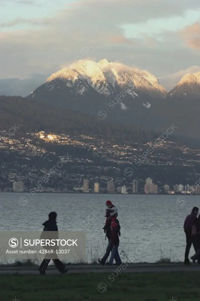 Walkers silhouetted against Burrard Inlet with North Vancouver and snow capped North Shore mountains behind