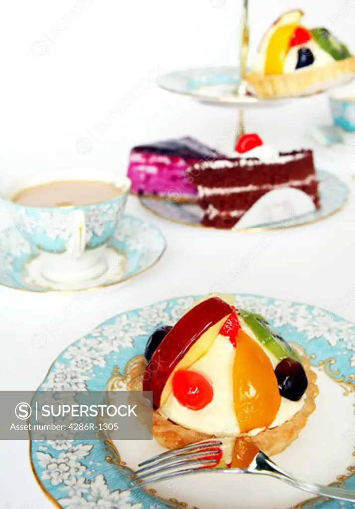 An elegant afternoon tea, in the English style,  with fruit tart and other cakes. High key, shallow depth of field