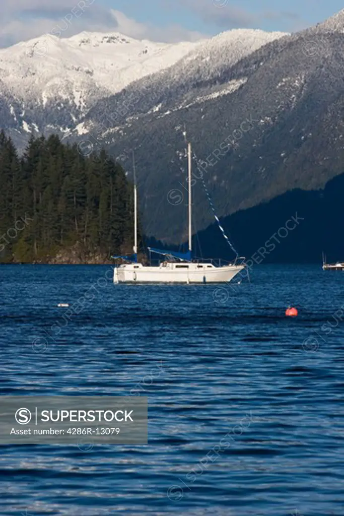 Sailboats anchored in Bedwell Bay, Indian Arm, Belcarra, BC, Canada. Snow covered Coast Mountains behind.