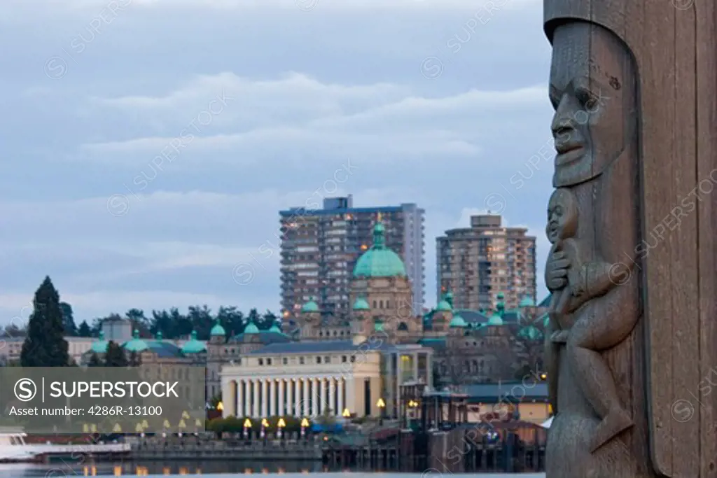 Totem Pole in foreground looks over inner harbour and Parliament Buildings - Victoria, BC, Canada