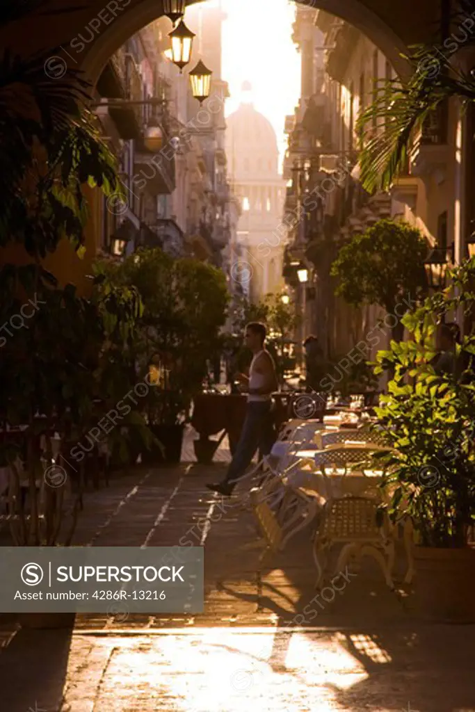 Late afternoon light streams in through archway into outdoor restaurant in Old Havana as man walks through