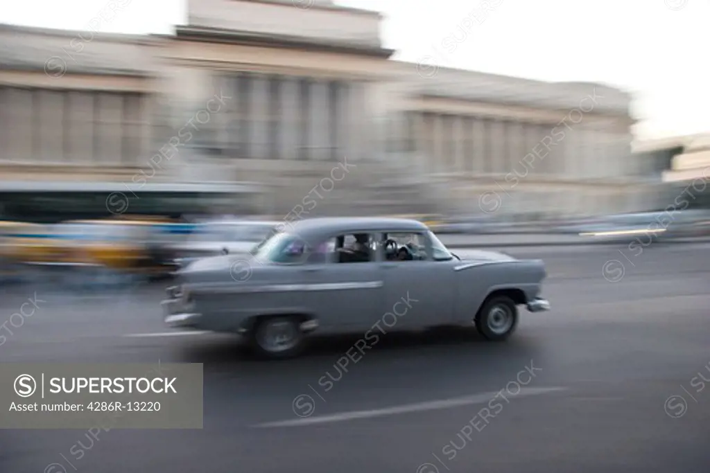 Old grey car whizzes down the street in front of the Capitolio in Old Havana
