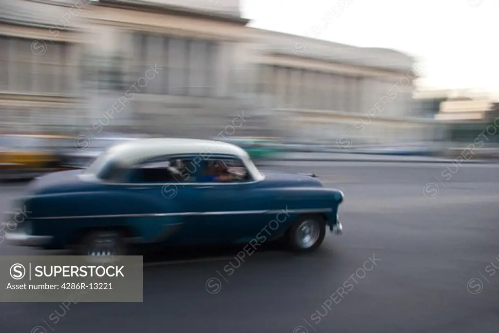 Classis car in motion down the street in front of the Capitolio in Old Havana