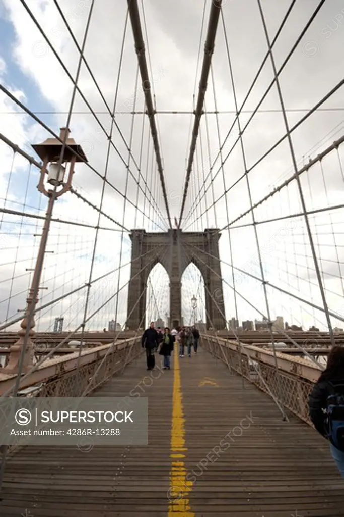 Tourists and commuters walk along the pedestrian deck of the Brooklyn Bridge, lower Manhattan, New York
