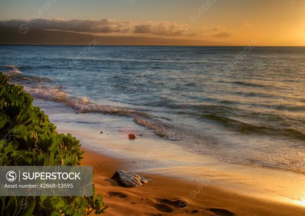 Sunsets warm glow on golden sand beach, West Maui, Hawaii. Island of Lanai in the distance