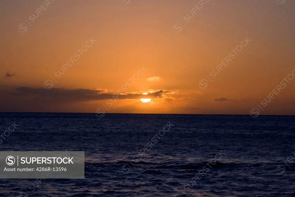 Maui sunset with setting sun partially covered by clouds, Hawaii