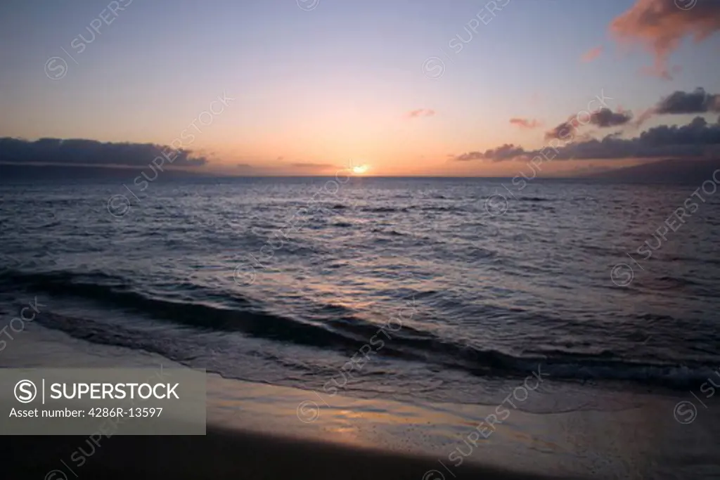 Maui beach sunset with setting sun partially covered by clouds, Hawaii