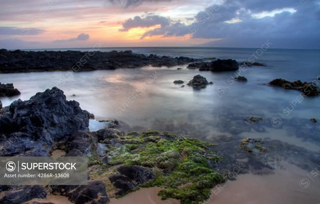 Volcanic rocks and tidepools at sunset, Napili Beach, Maui. Island of Molokai is in the distance