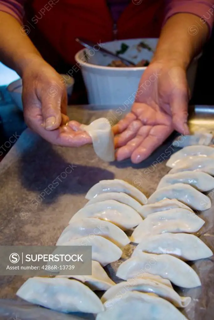 Chinese cook demonstrating how to make wor tip, also known as potstickers or pork dumplings