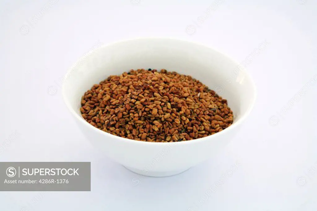 A bowl of fenugreek seeds, spices used in curries, on a white background