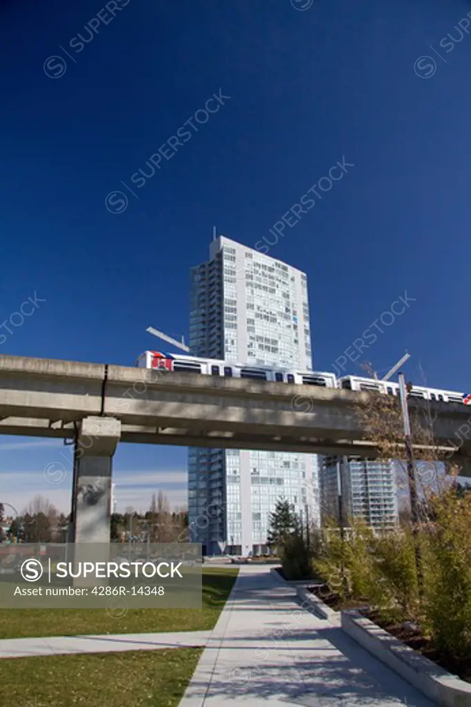 Skytrain passes in front of modern apartment building, Holland Park, Surrey Central, BC, Canada