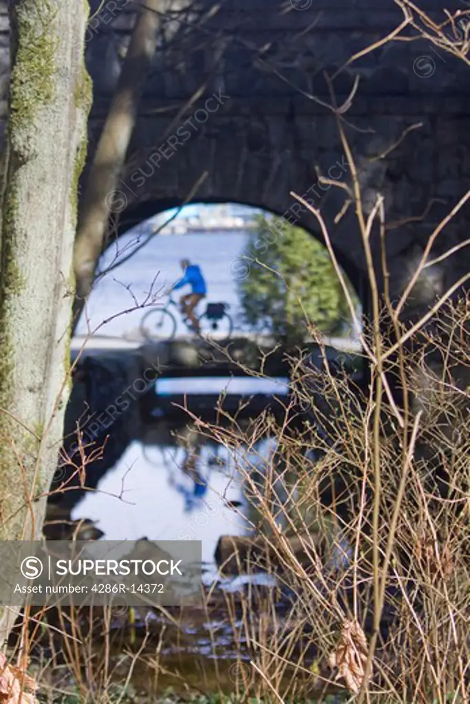 Cyclist passes along seawall, as seen through tunnel. Stanley Park, Vancouver BC, Canada