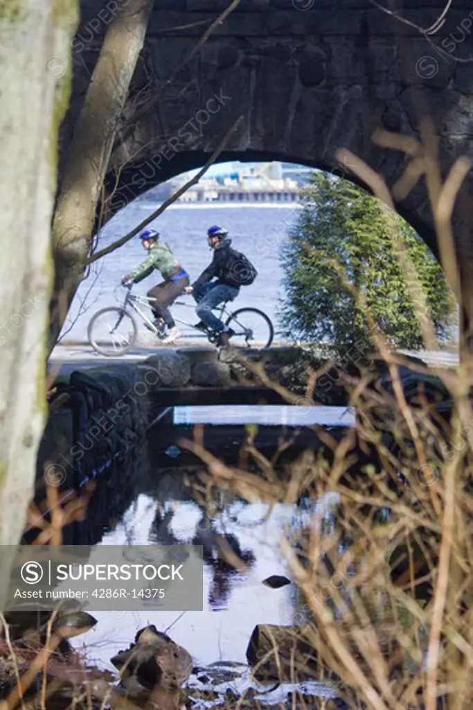 Couple on tandem bike along seawall, as seen through tunnel. Stanley Park, Vancouver BC, Canada