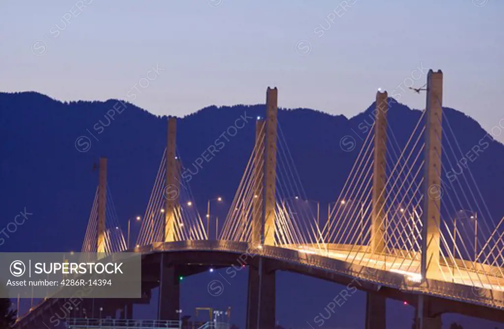 Golden Ears Bridge lit up at night. Coast Mountains behind.
