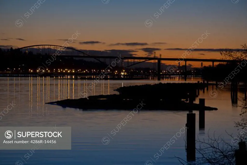 Log booms on Fraser River and Port Mann Bridge on a clear night at dusk, Port Coquitlam, BC, Canada.