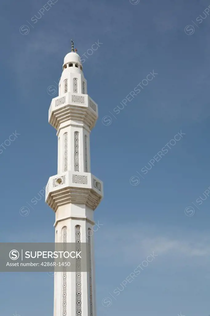 The minaret of a mosque in Qatar, against a slightly cloudy blue sky.
