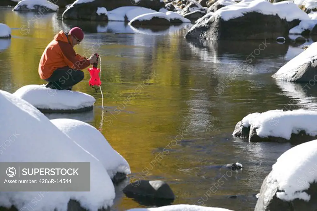 A man filling a water bottle on a snowy river in the fall in the Sierra mountains of California.