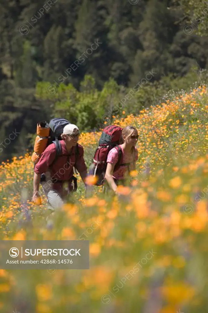 A man and woman backpacking in spring on a trail lined with flowers near Auburn, CA.