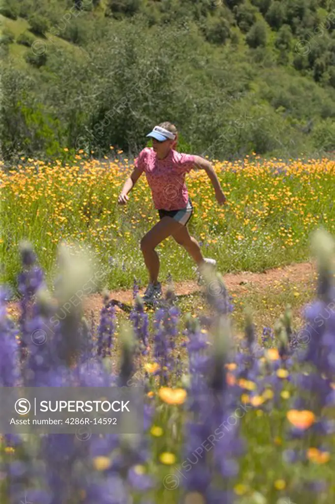 A woman running in spring on a trail lined with flowers near Auburn, CA.