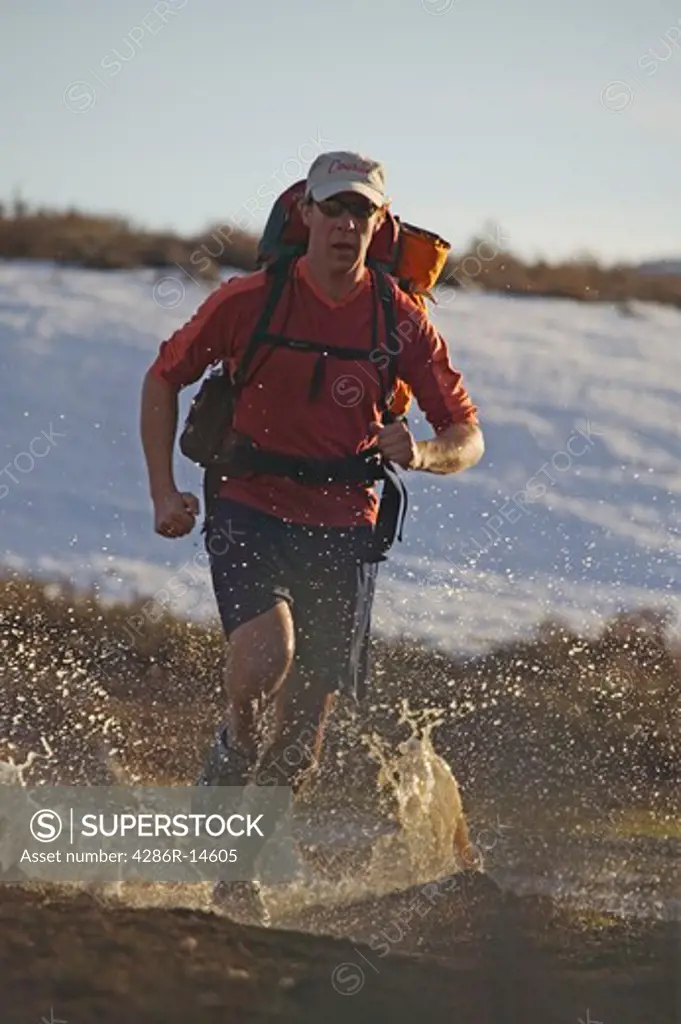 A man running while backpacking on a trail covered with water near Truckee, CA.