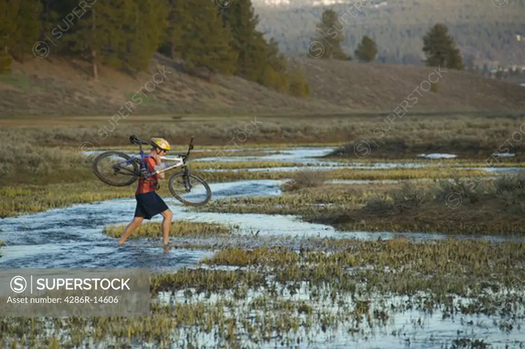 A man carrying his bike across a stream while mountain biking near Truckee, CA.