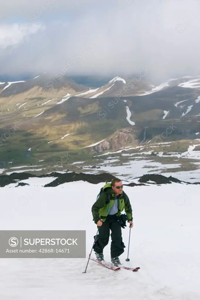 A skier climbing Mount Vsevidov in Alaska with green tundra below.