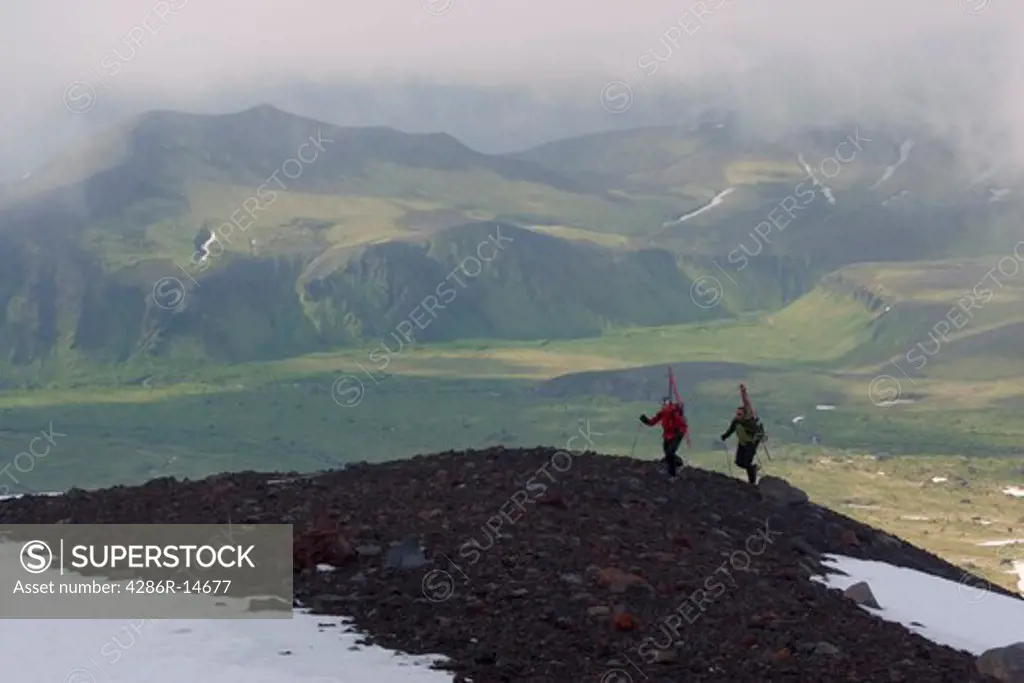 Two skiers climbing Mount Vsevidov in the Aleutian islands above green tundra.