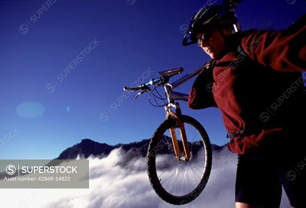 A woman carrying her bike while mountain biking above the clouds near Truckee, CA.