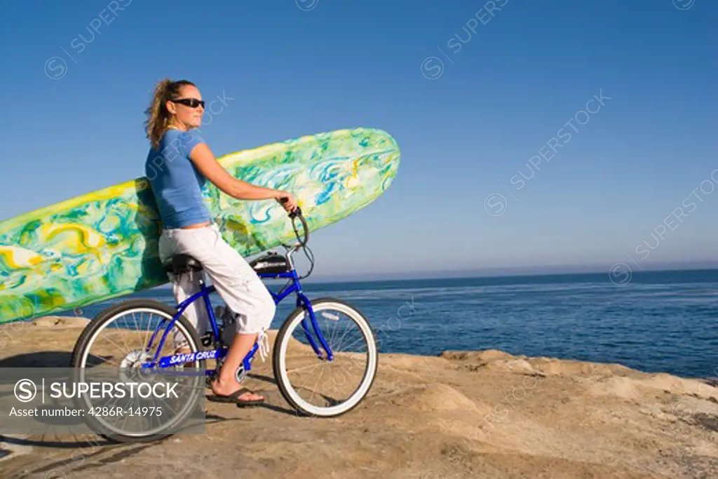 A woman with a bike and surfboard on the beach at sunset at Natural Bridges State Park in Santa Cruz California