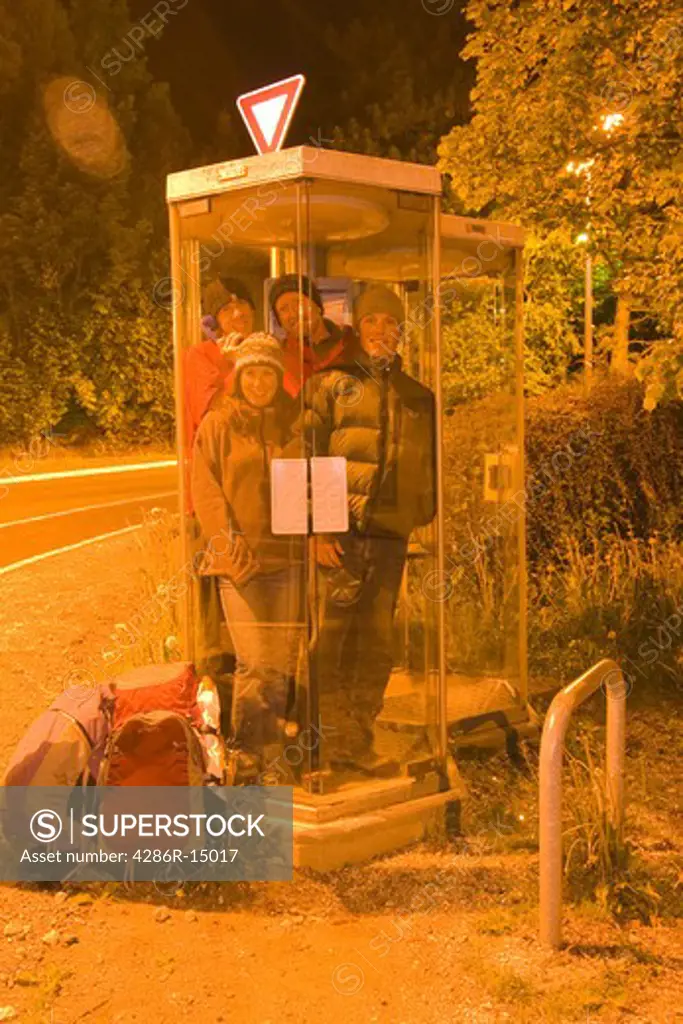 Four friends in a phone booth at night in Chamonix France.