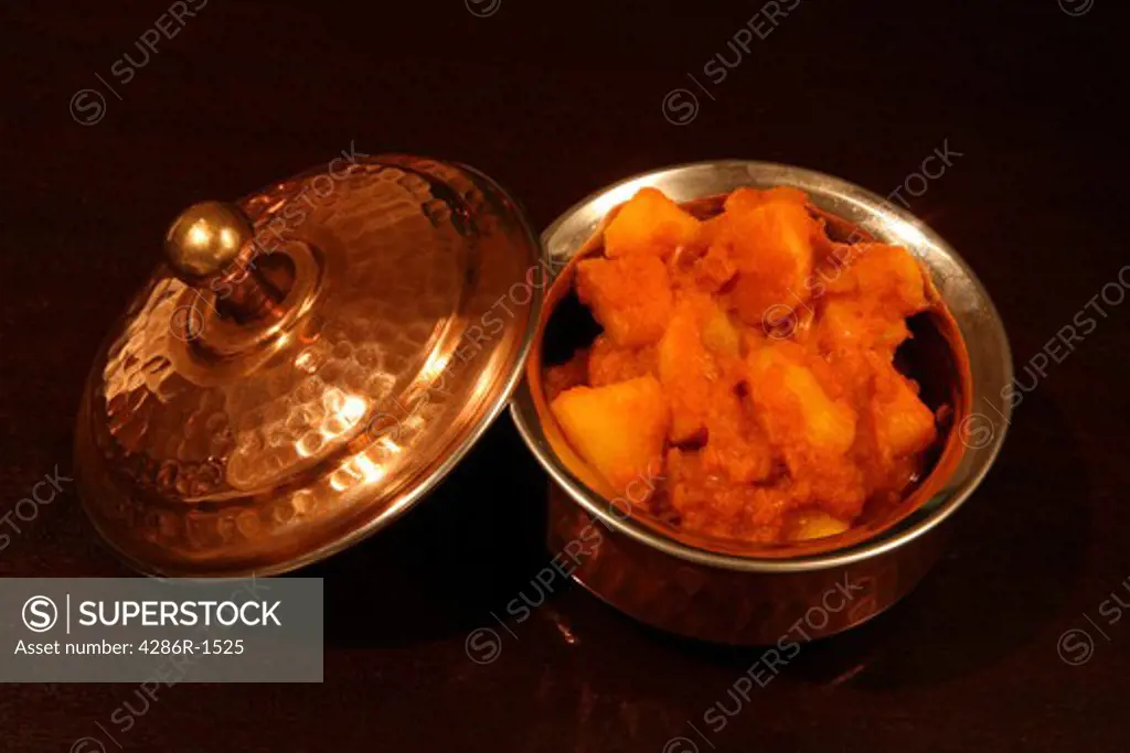 An authentic Indian copper-clad serving bowl containing Punjabi potato curry, a north-Indian favourite, on a dark wood table.