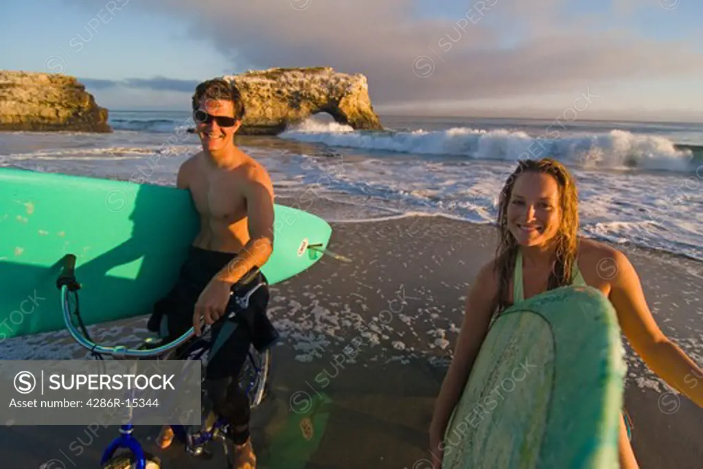 A couple with bikes and surfboards on the beach at sunset at Natural Bridges State Park in Santa Cruz California