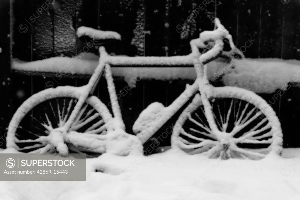 A bicycle covered with snow next to a fence.
