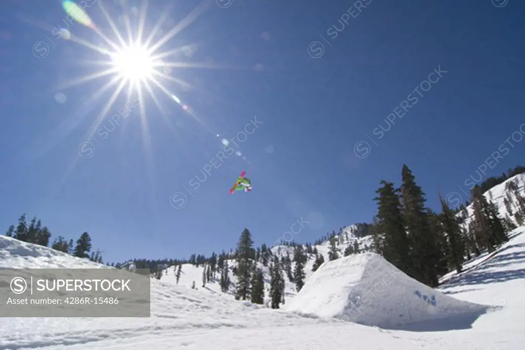 A snowboarder jumping off a jump with a sunburst at Alpine Meadows in California