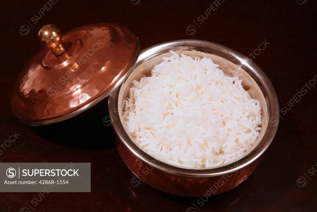 A bowl of white rice in a traditional asian serving dish on a dark table.