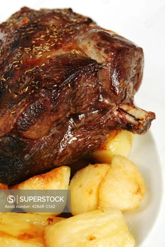 A roasted leg of lamb on a plate with roast potatoes.