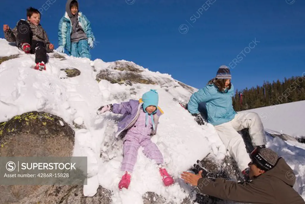 Four children sliding off a snowy rock at Sierra at Tahoe ski resort near Lake Tahoe in California