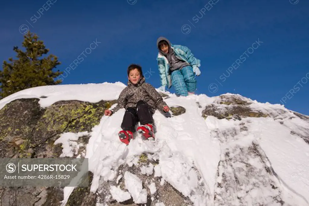 A girl and boy sliding off a snowy rock at Sierra at Tahoe ski resort near Lake Tahoe in California