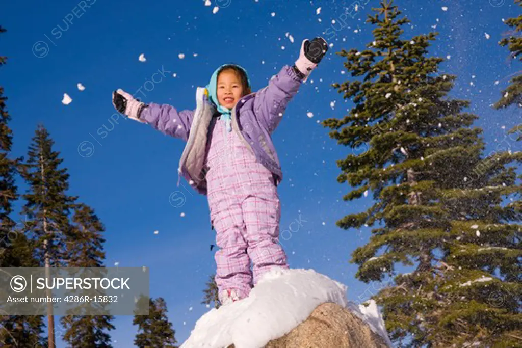 A victorious girl standing on top of a snowy rock at Sierra at Tahoe ski resort near Lake Tahoe in California