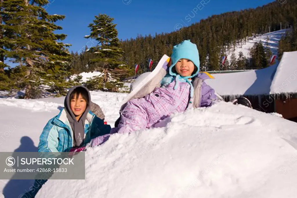 Two girls climbing on a snowy rock at Sierra at Tahoe ski resort near Lake Tahoe in California