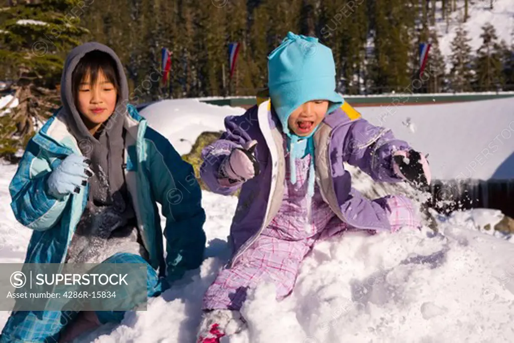 Two girls climbing on a snowy rock at Sierra at Tahoe ski resort near Lake Tahoe in California