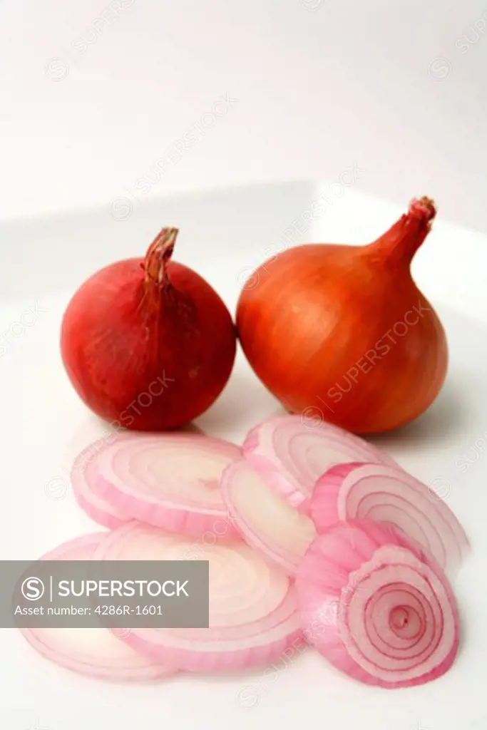 Slices of onion, with two onions behind them, on a plate.