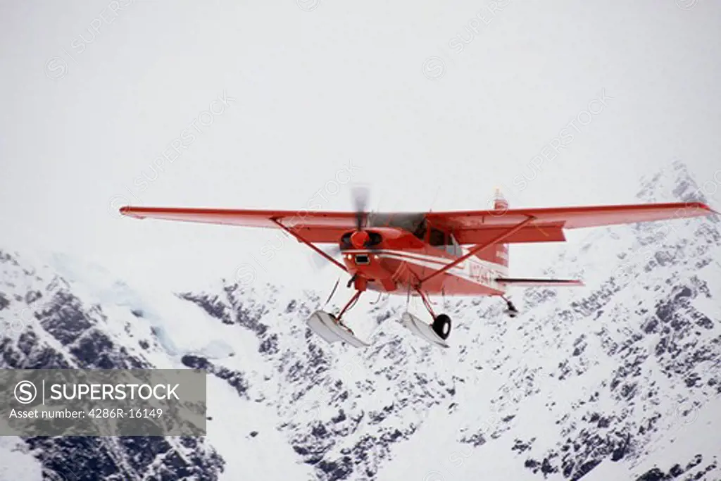 A bush plane with skis flying through the mountains of the Alaska Range in Alaska near Denali