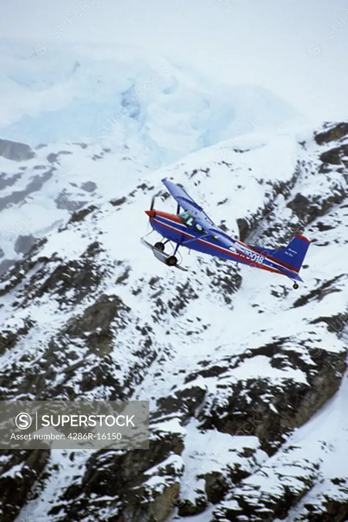 A bush plane with skis flying through the mountains of the Alaska Range in Alaska near Denali