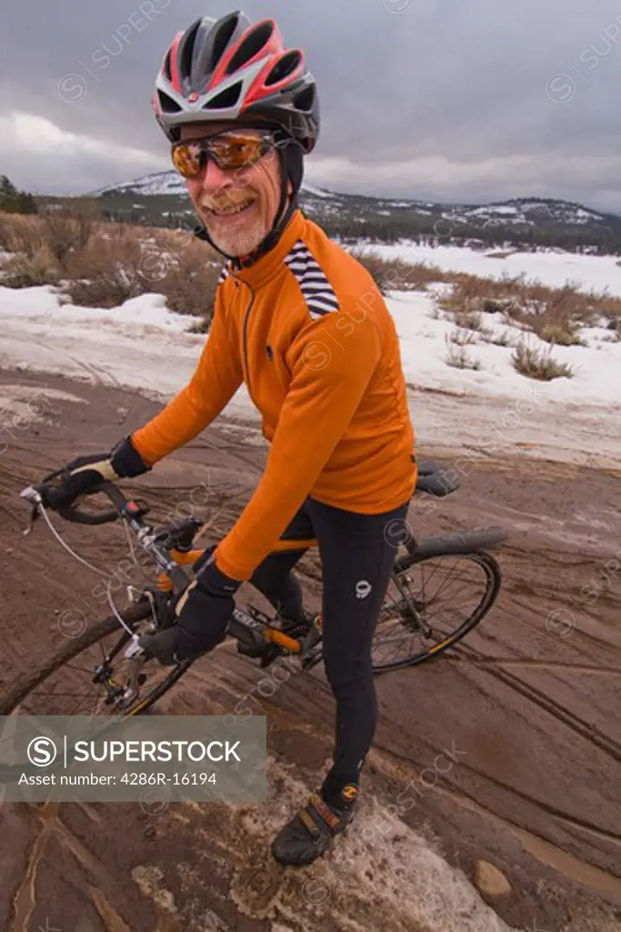 a man with a cyclocross bicycle in mud on an overcast winter day