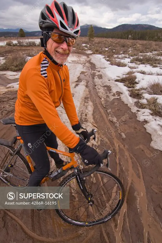 a man with a cyclocross bicycle in mud on an overcast winter day