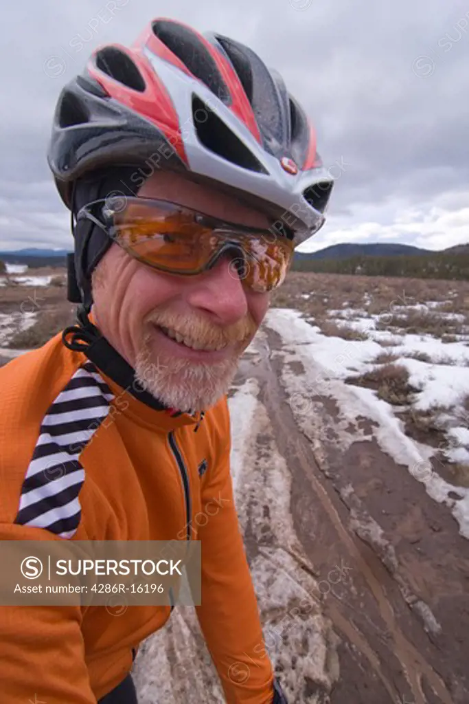 a man wearing a bicycle helmet and orange jersey on an overcast day on a muddy and snowy dirt road